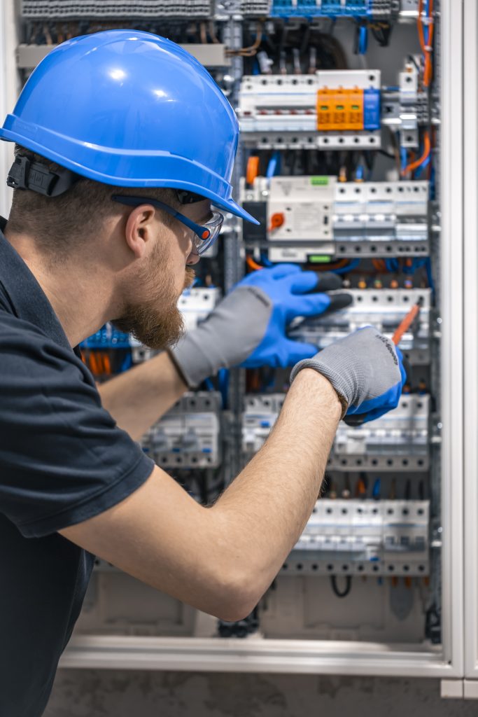 a male electrician works in a switchboard with an electrical connecting cable.
