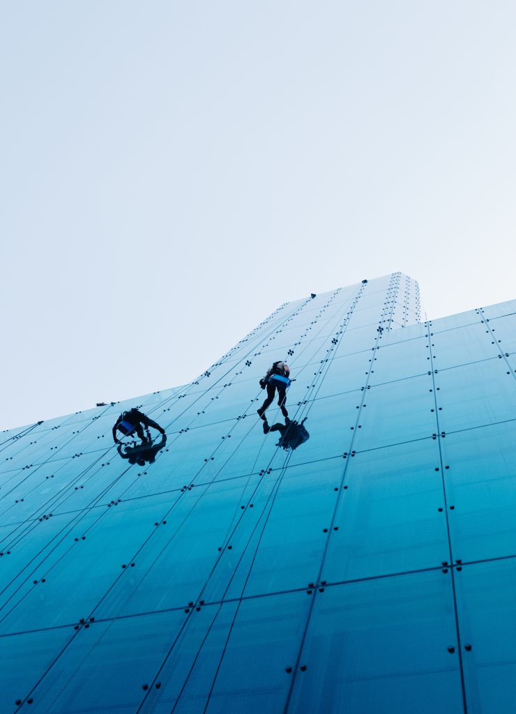 vertical low angle shot of two people climbing a tall glass building during the day time