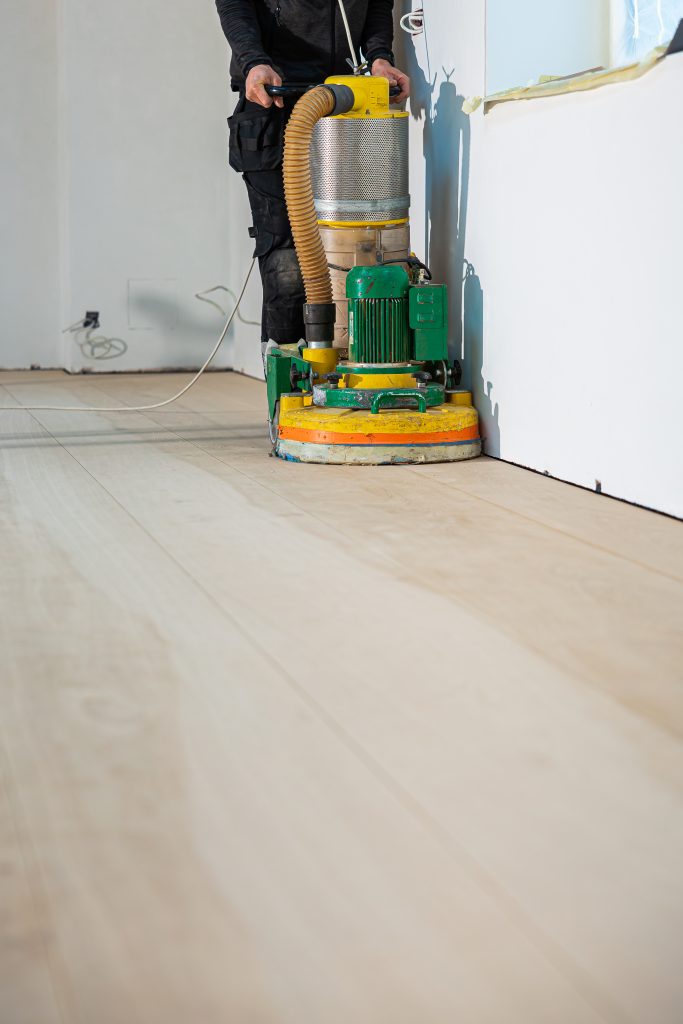 worker sanding light colored wooden floor with green and yellow machine