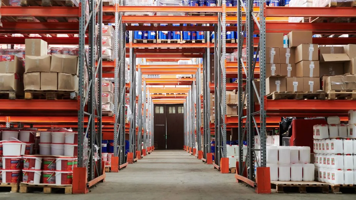 Allée d'entrepôt bordée de rayonnages chargés de palettes, de bidons et de cartons