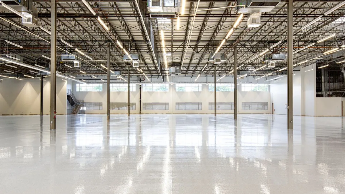 Hall industriel vide au sol en résine brillante, sous une charpente métallique éclairée