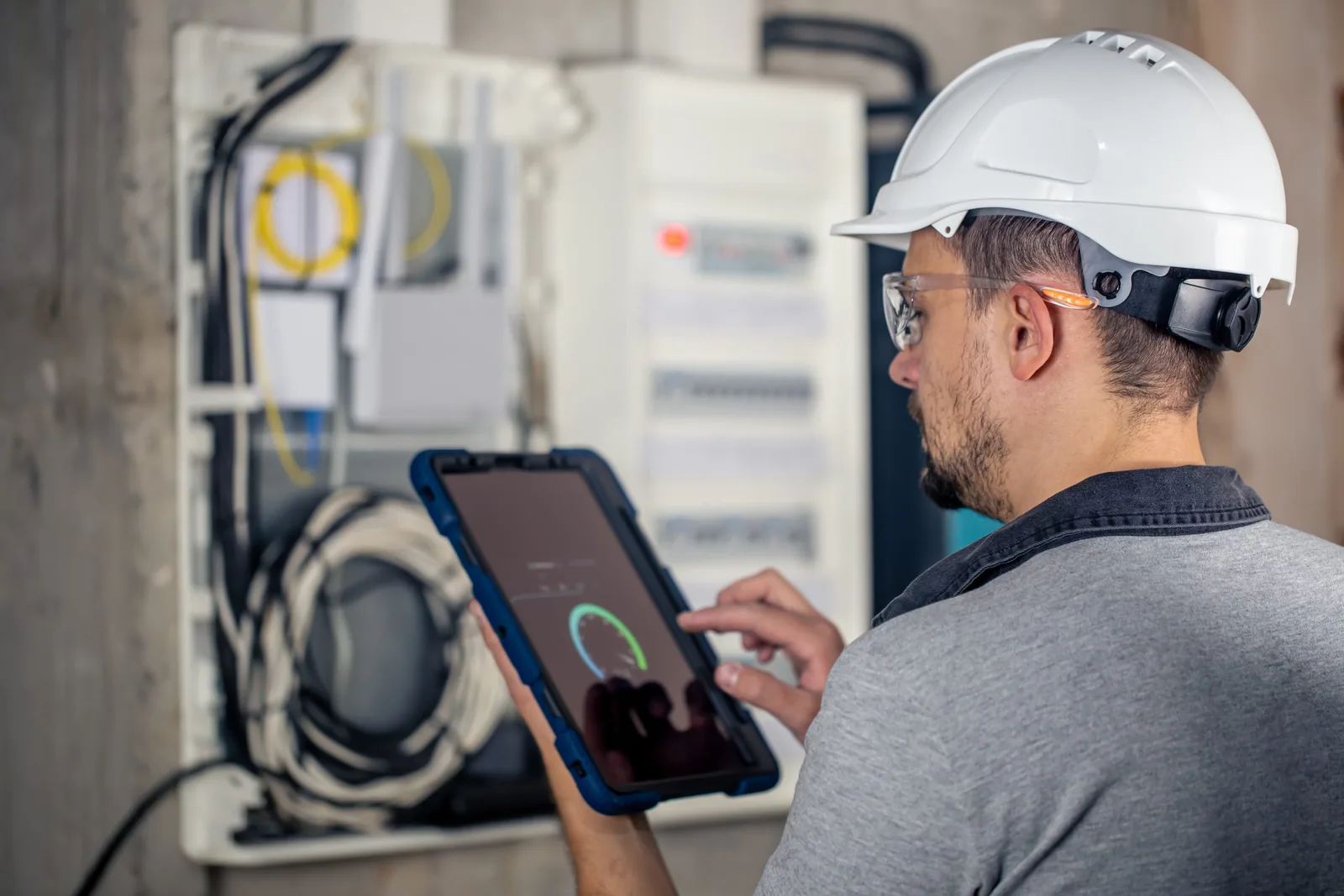Technicien casqué consultant une tablette devant une armoire électrique