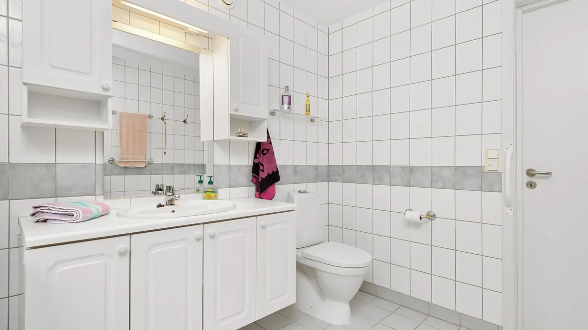 Salle de bain carrelée de blanc, avec lavabo, miroir et éclairage intégré