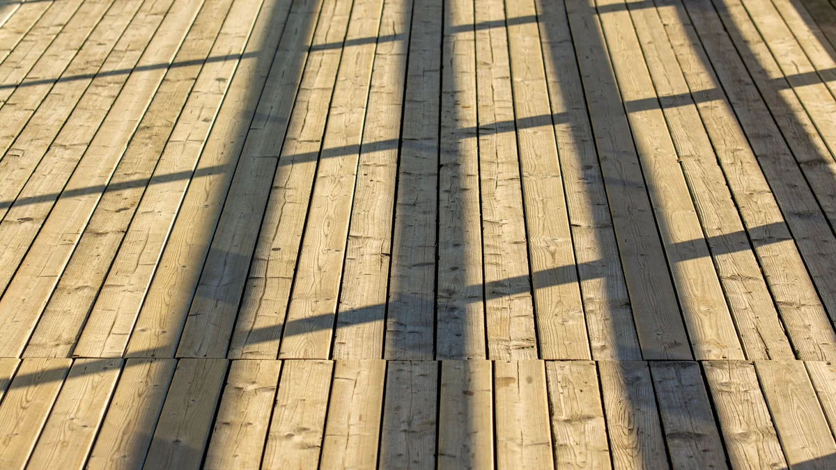 Terrasse en bois clair au soleil, ombres du garde-corps portées sur les lames