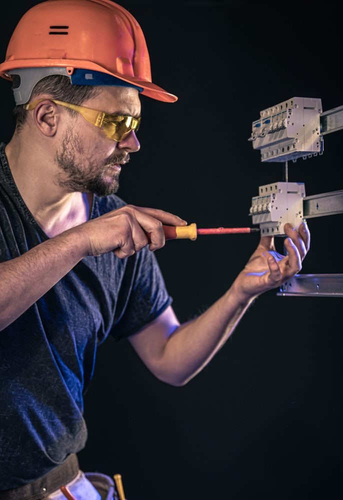 a male electrician works in a switchboard with an electrical connecting cable.